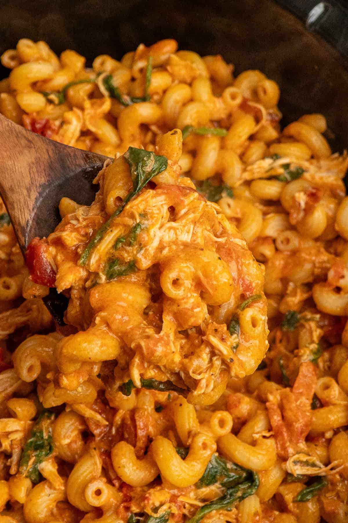 A wooden spoon holding a scoop of marry me chicken pasta.