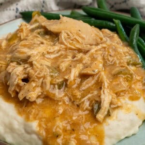 Crock pot smothered chicken over mashed potatoes on a plate with green beans.