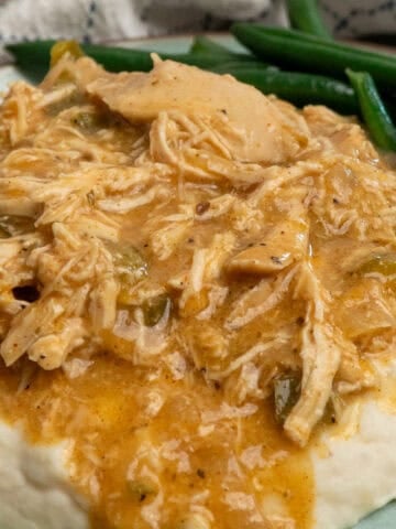 Crock pot smothered chicken over mashed potatoes on a plate with green beans.