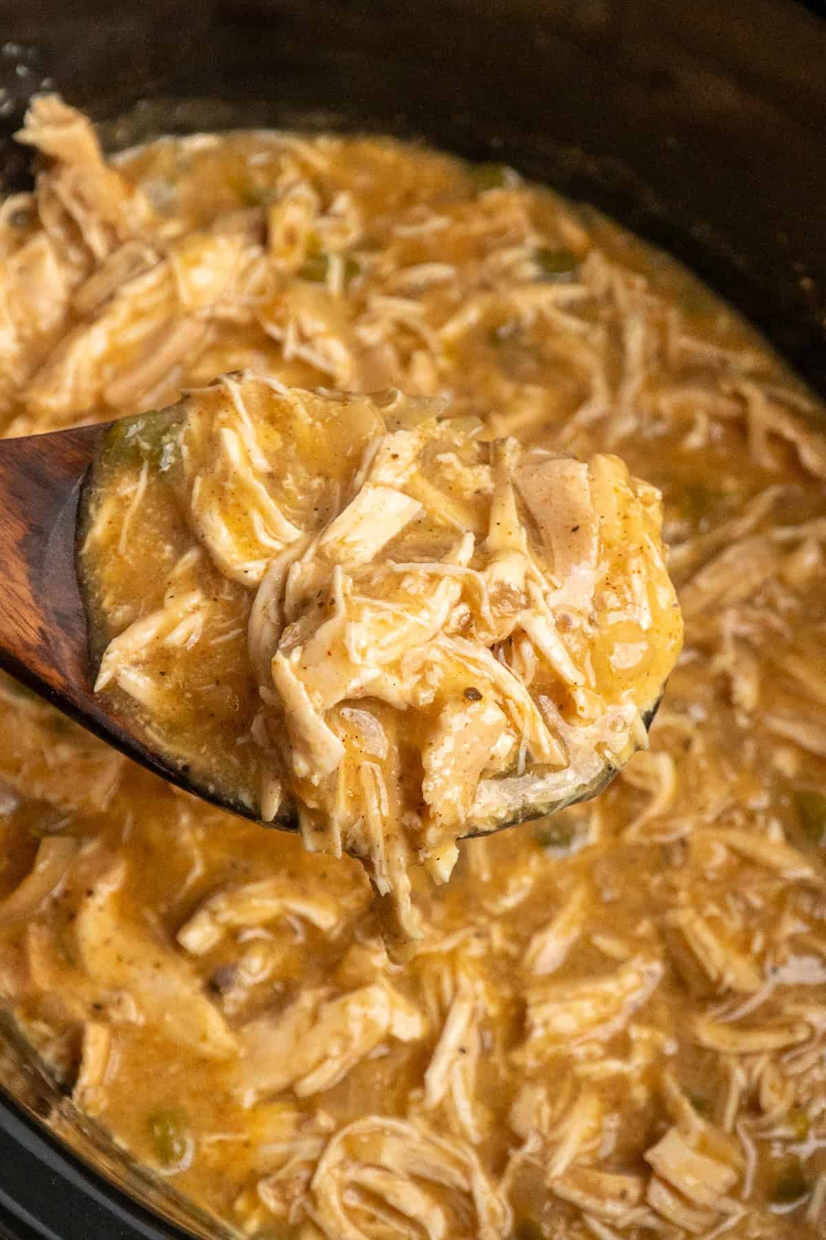 A wooden spoon holding a scoop of smothered chicken over a crock pot.