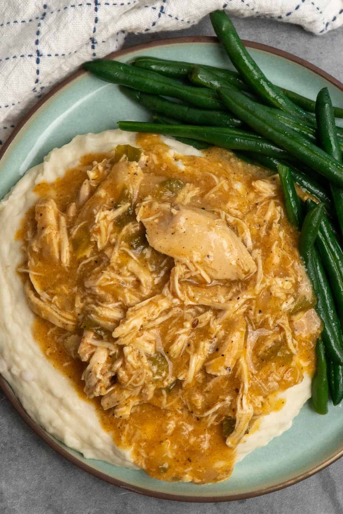 Crock pot smothered chicken over mashed potatoes on a plate with green beans.