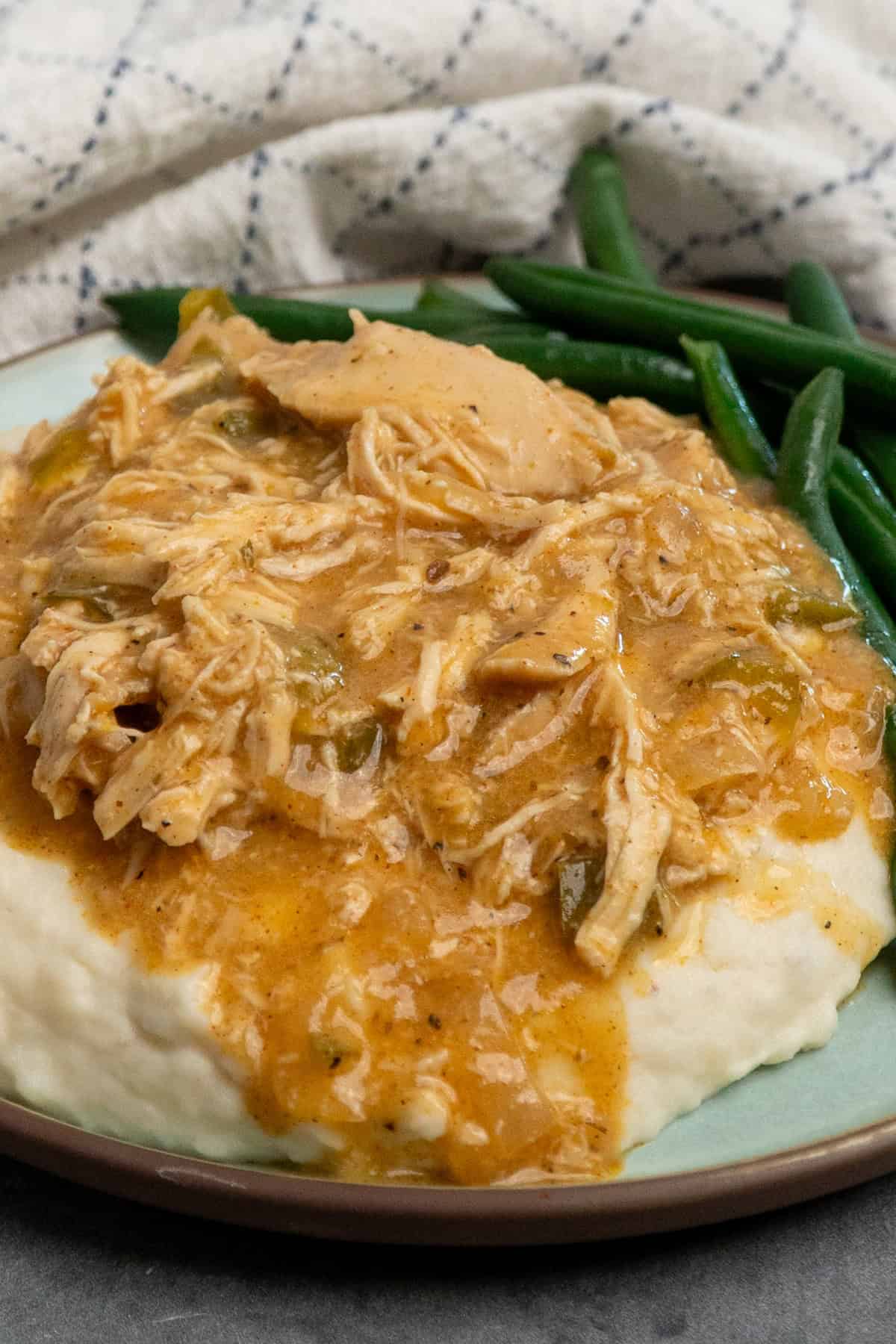 Crock pot smothered chicken over mashed potatoes on a plate with green beans.