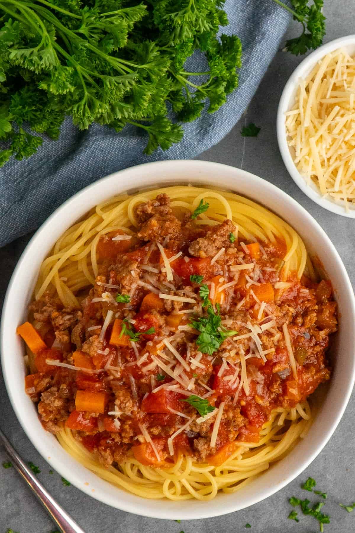 Slow cooker bolognese sauce over spaghetti noodles with parsley in the background.