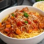 Slow cooker bolognese over a bowl of noodles and garnished with parmesan.