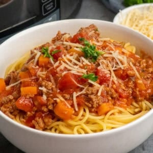 Slow cooker bolognese over a bowl of noodles and garnished with parmesan.