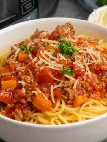 Slow cooker bolognese over a bowl of noodles and garnished with parmesan.