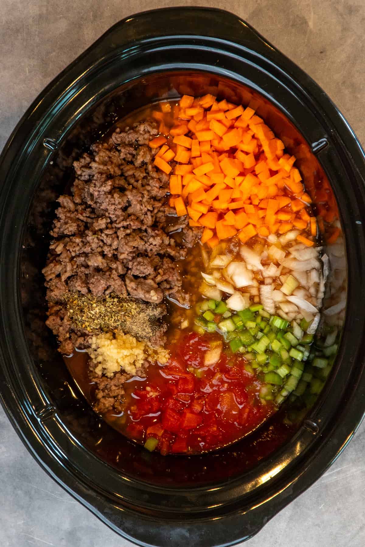 All the ingredients for bolognese in a slow cooker ready to be cooked.