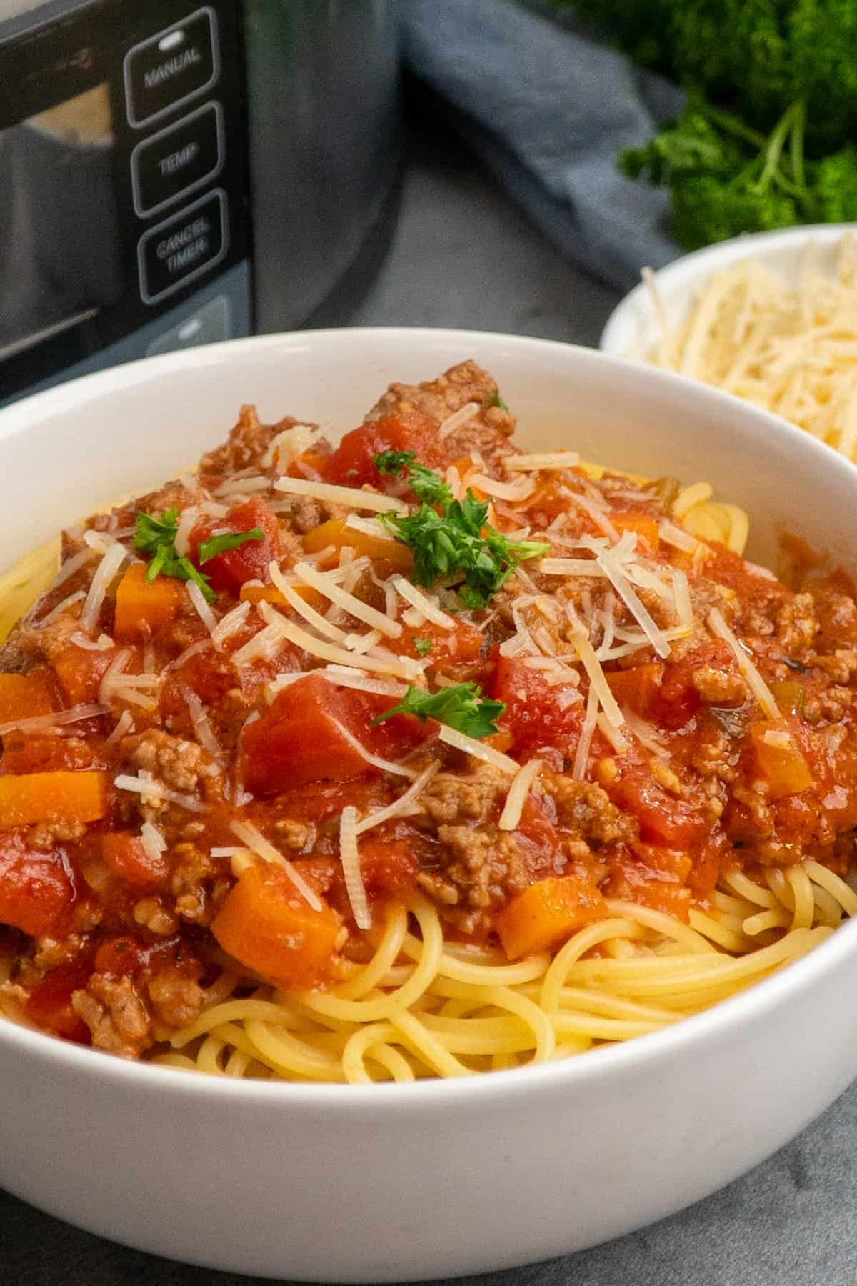 Slow cooker bolognese over a bowl of noodles and garnished with parmesan.