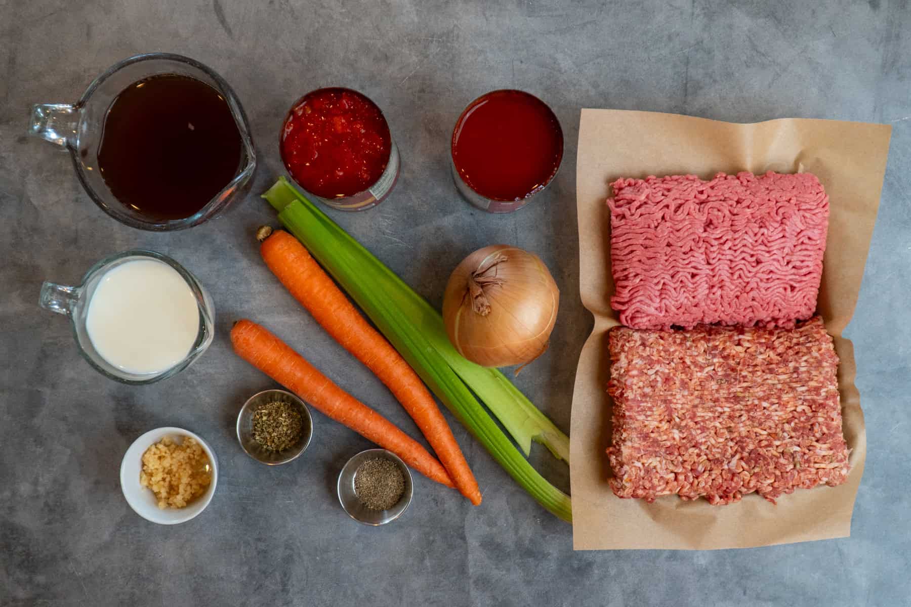 Ingredients to make bolognese sauce on a gray countertop.