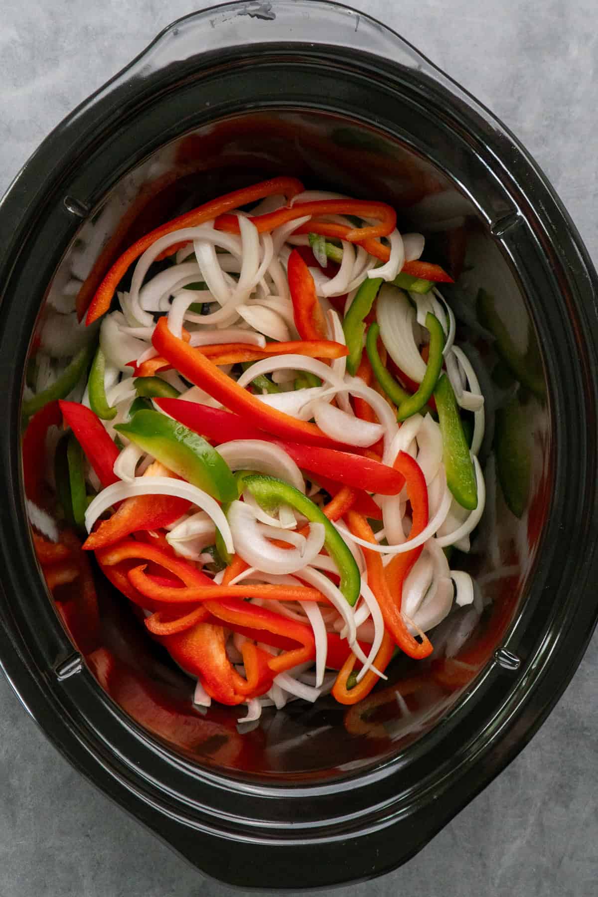 Sliced onions and bell peppers in a slow cooker.