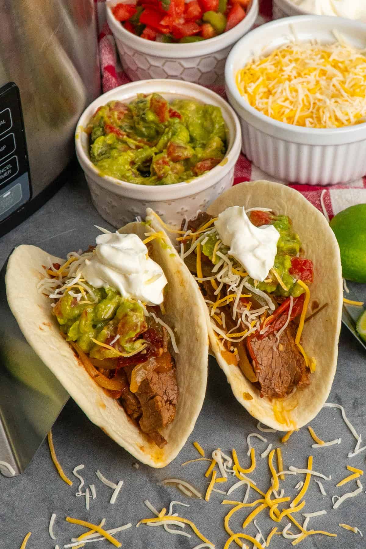 Two steak fajitas in tortillas and topped with cheese, guacamole, and sour cream.