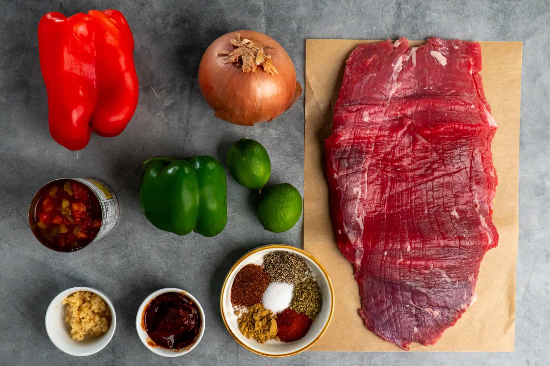 Ingredients to make steak fajitas on a gray countertop.