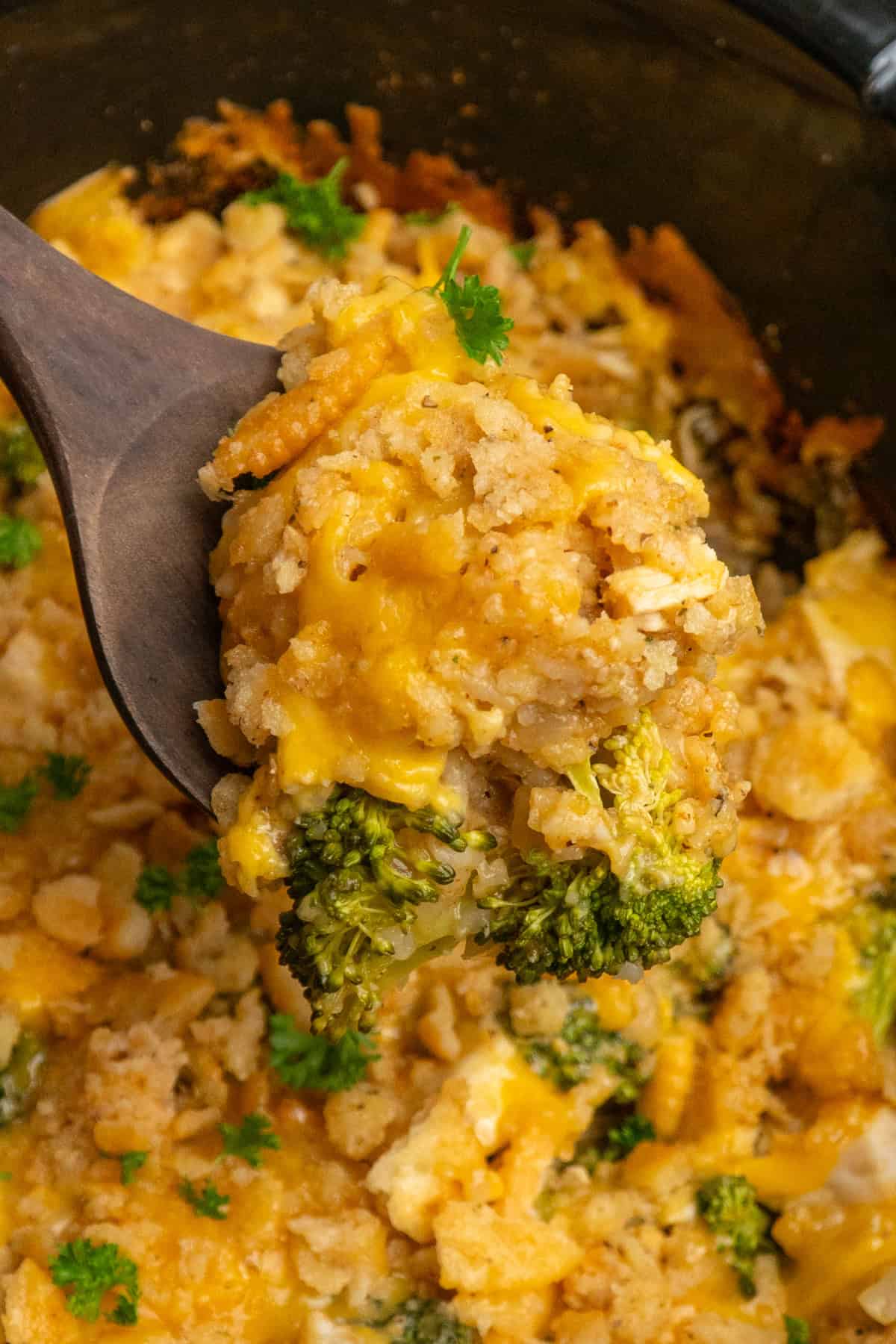 A wooden spoon holding a scoop of crock pot chicken broccoli and rice casserole.