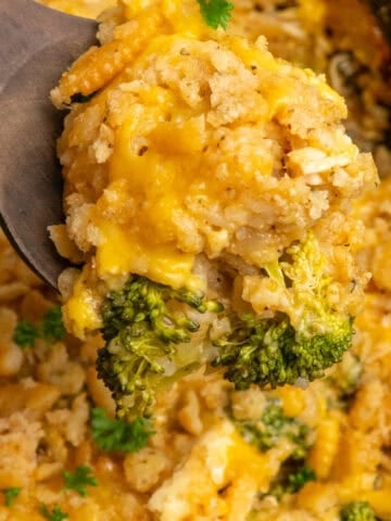 A wooden spoon holding a scoop of crock pot chicken broccoli and rice casserole.