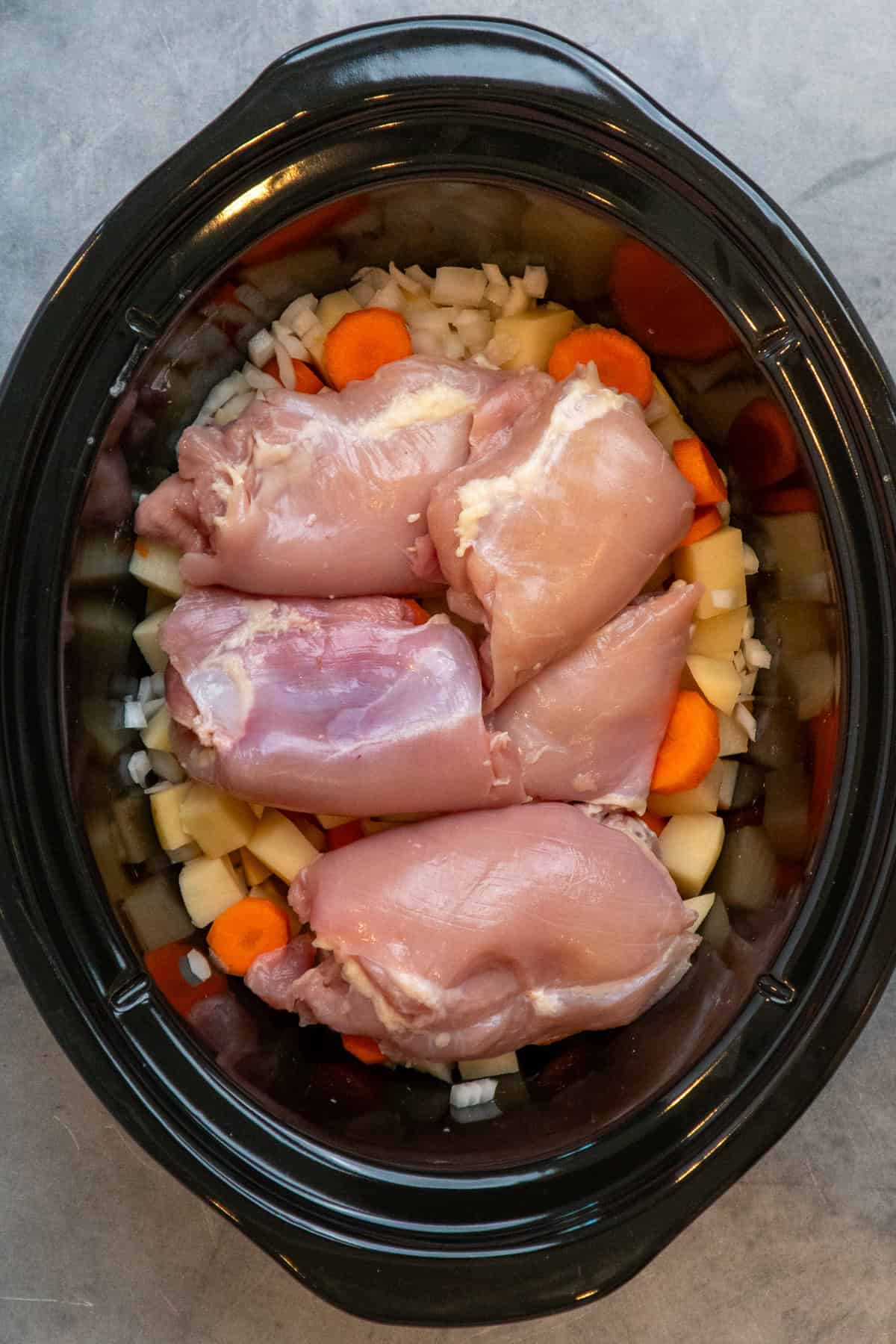 Chicken added on top of the vegetables in a slow cooker.