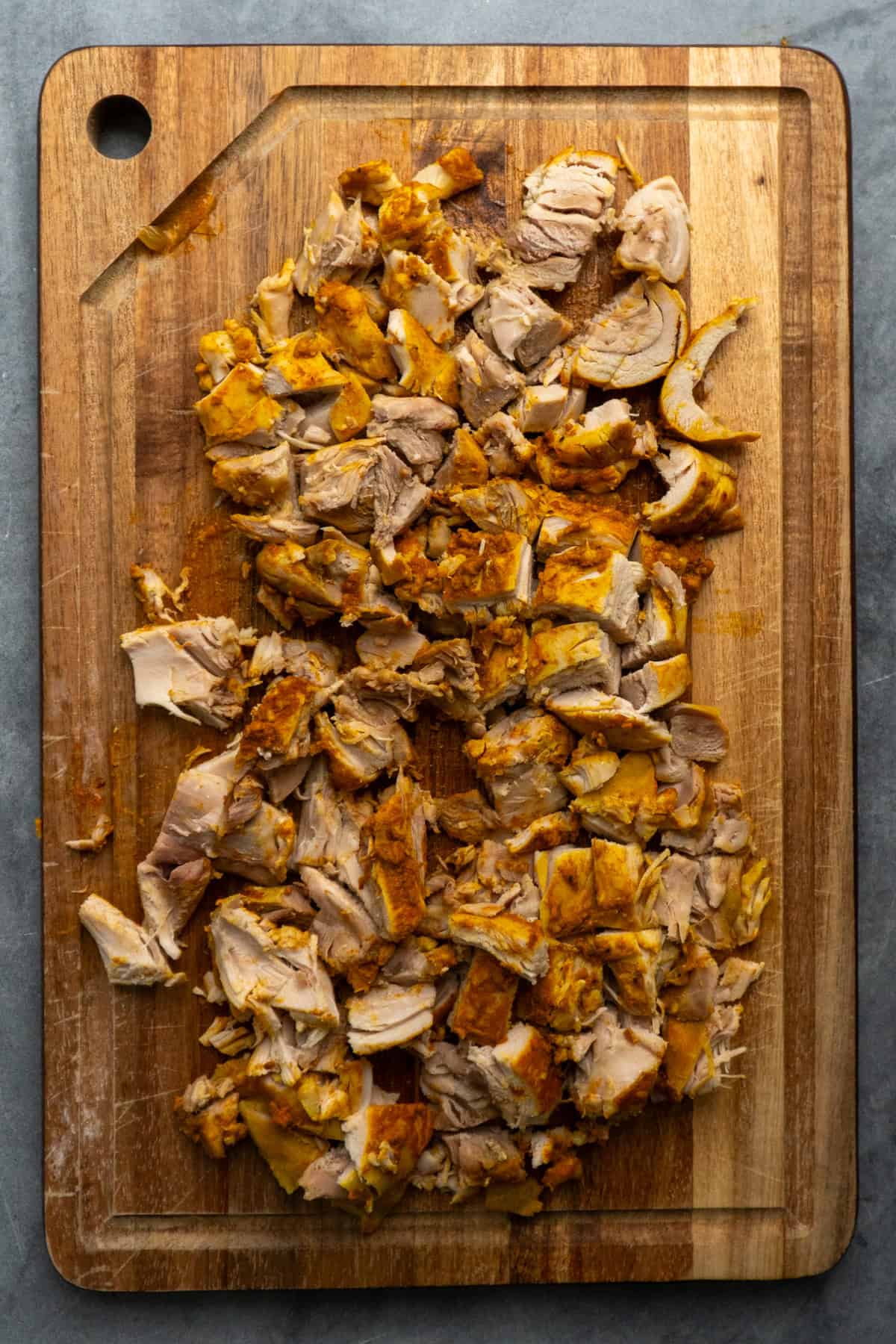 Coconut curry chicken diced into pieces on a wooden cutting board.