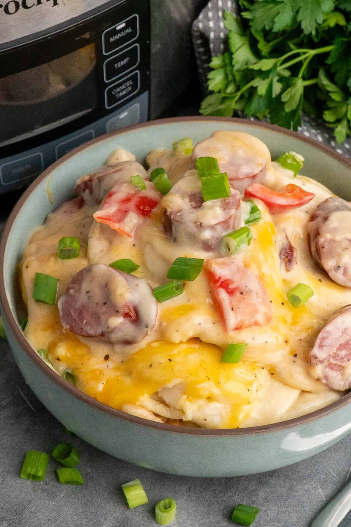 Crock pot pierogi casserole in a blue bowl and garnished with green onions.