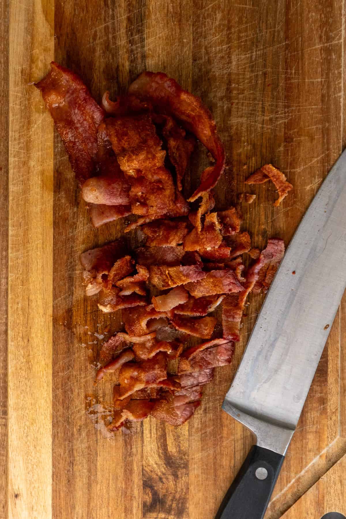 Bacon that has been cooked and chopped on a wood cutting board.