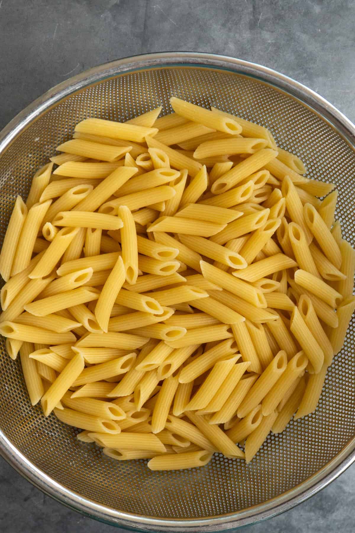 Cooked penne pasta in a  in a colander ready to be added to the cooked chicken.