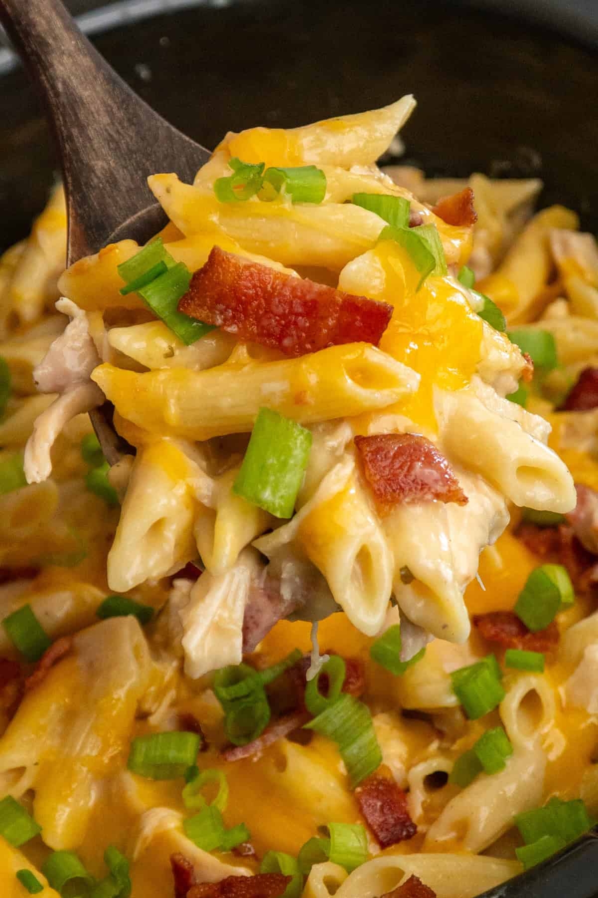 A wooden spoon holding a scoop of crack chicken pasta over a crock pot.