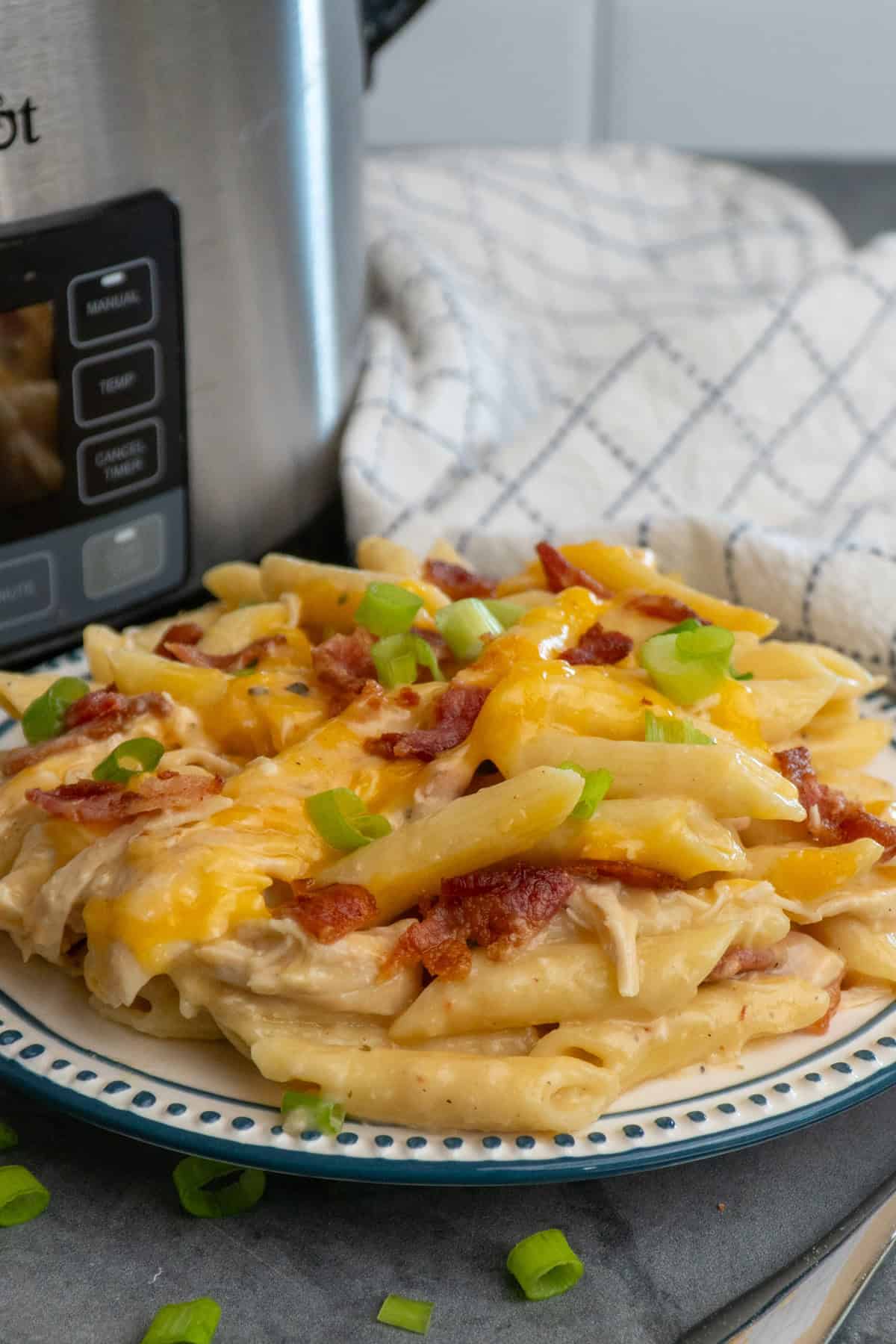 Crack chicken pasta on a plate with a crock pot in the background.