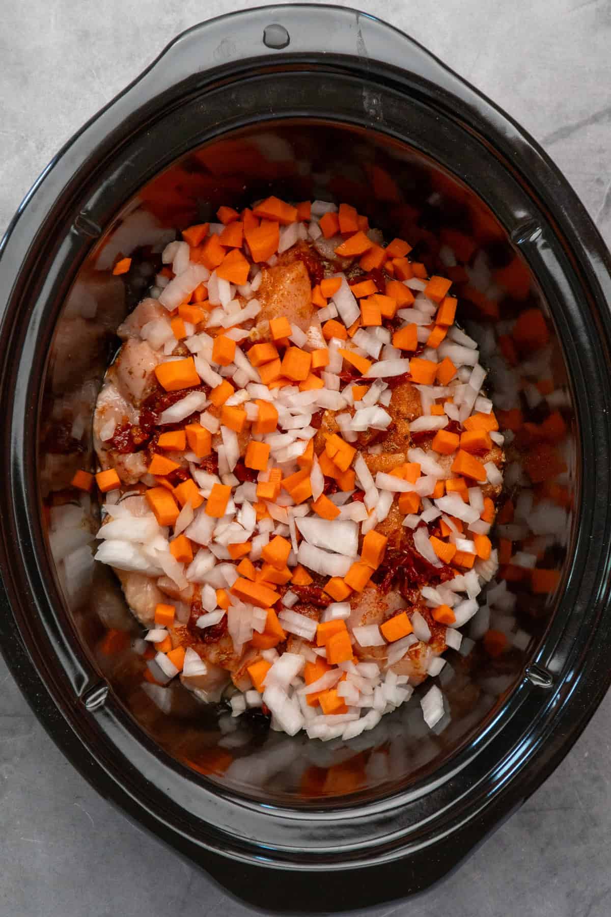 Cubed chicken breasts, chicken broth, seasonings, onion, carrots, and sun dried tomatoes in a crock pot.