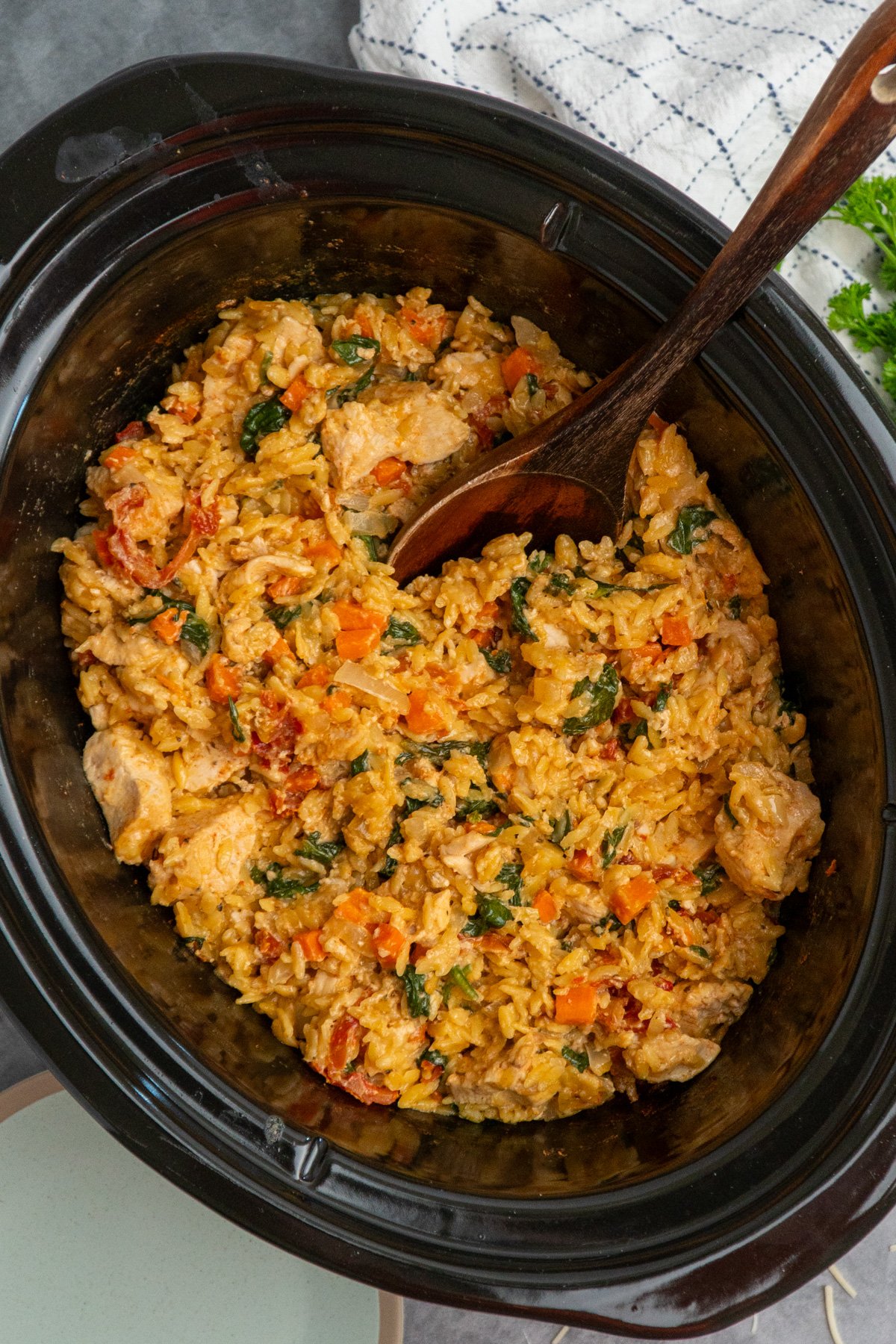 A wooden spoon in a crock pot full of marry me chicken orzo.