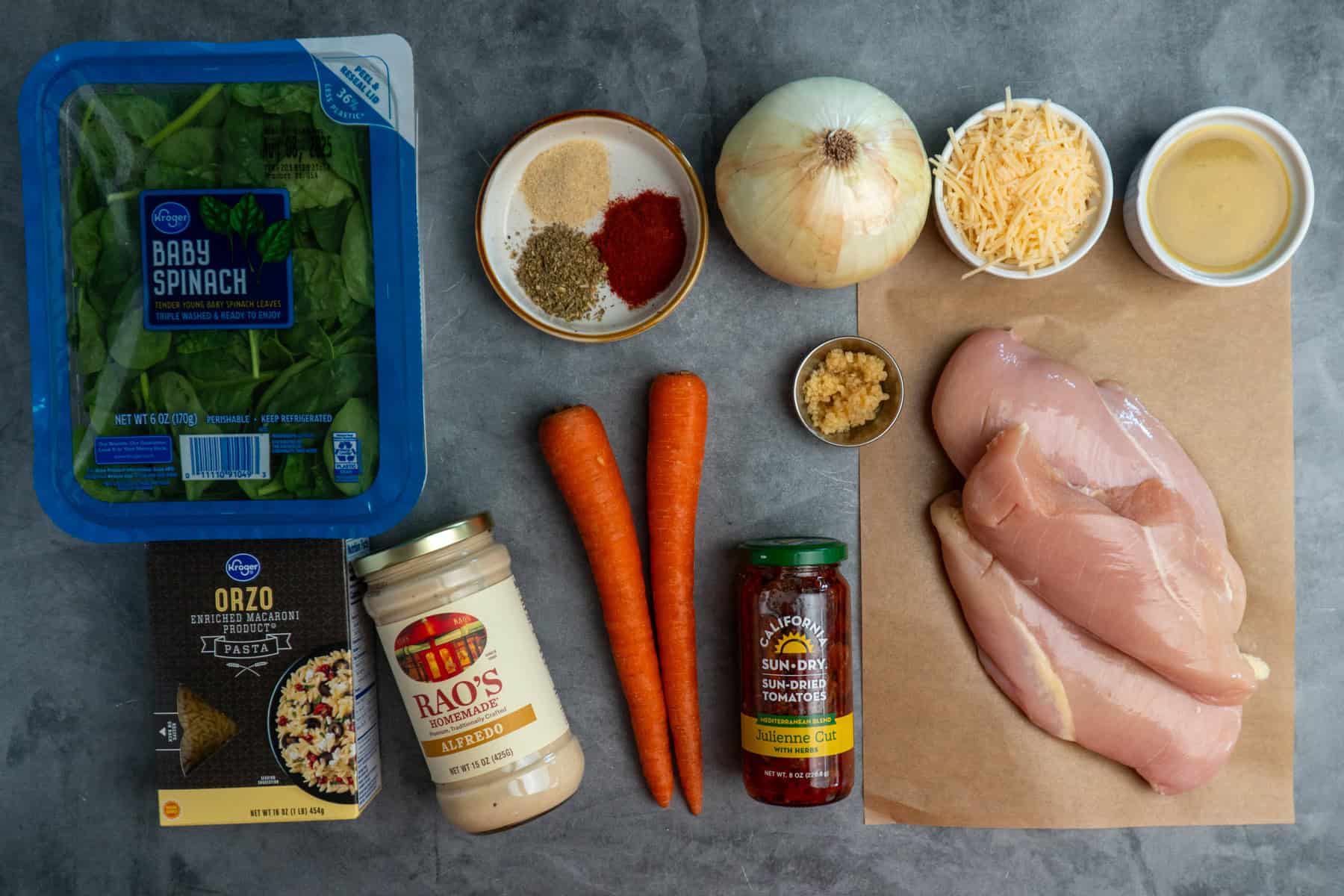 All the ingredients to make marry me chicken orzo on a gray stone countertop.