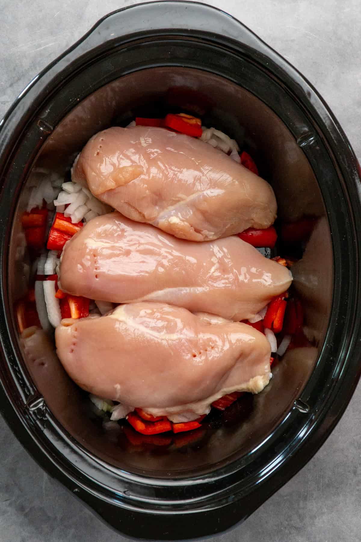 Onions, red bell peppers and three chicken breasts in a crock pot.