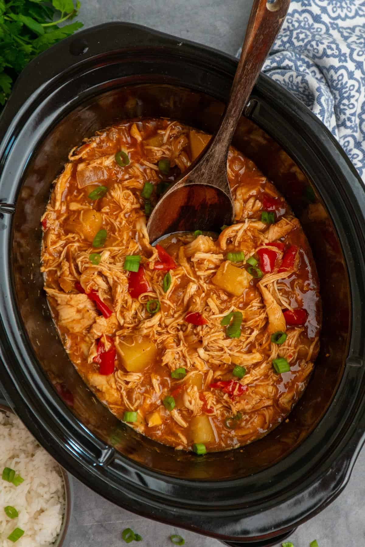 Pineapple BBQ chicken in a crock pot with a wooden spoon ready to be served.
