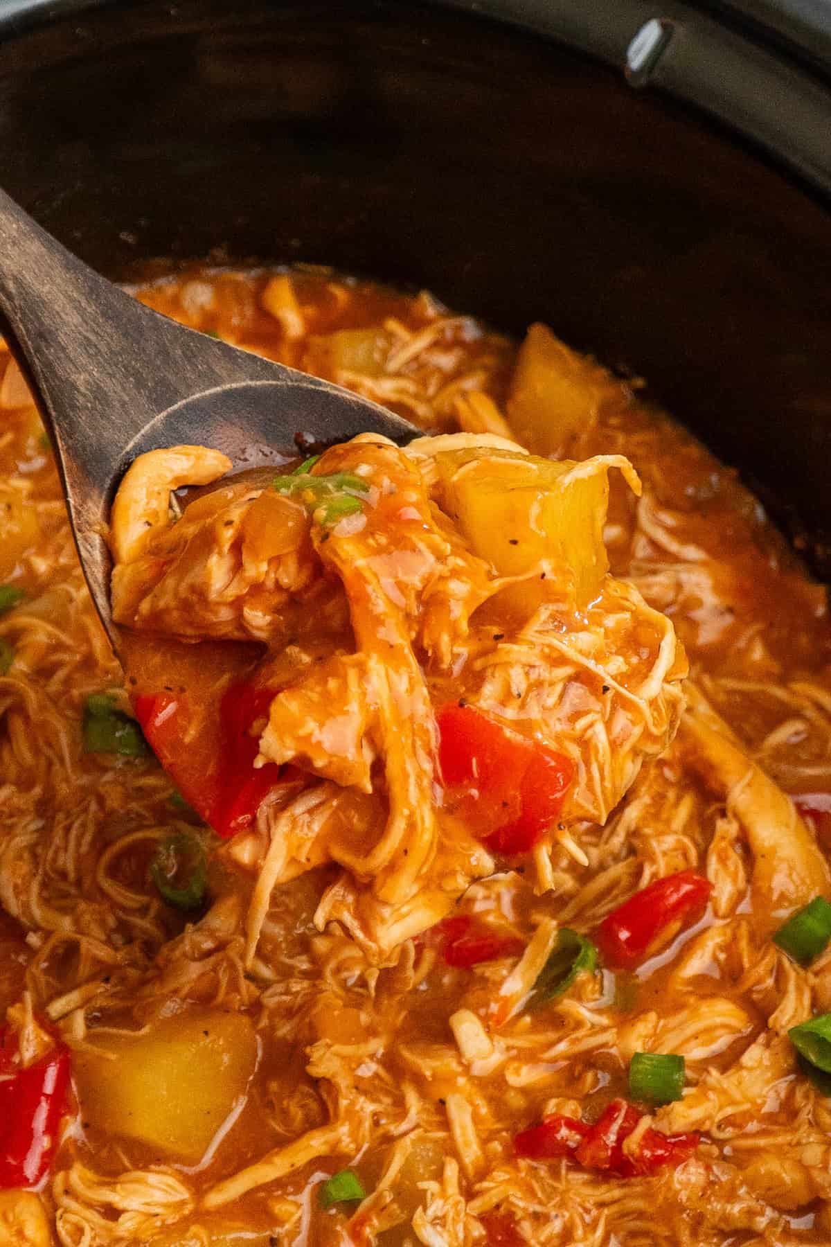 A wooden spoon holding  a scoop of pineapple BBQ chicken.
