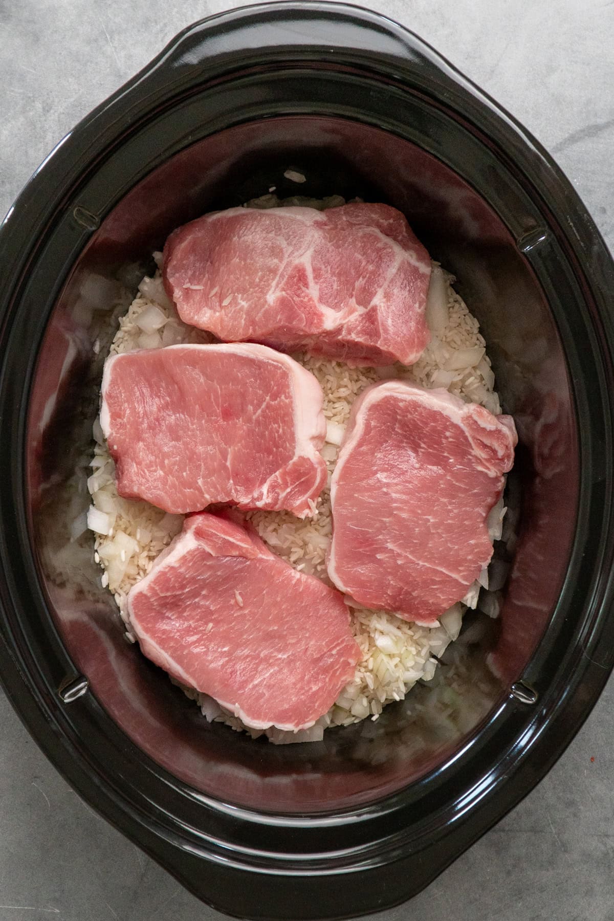 Uncooked pork chops and rice in a crock pot.