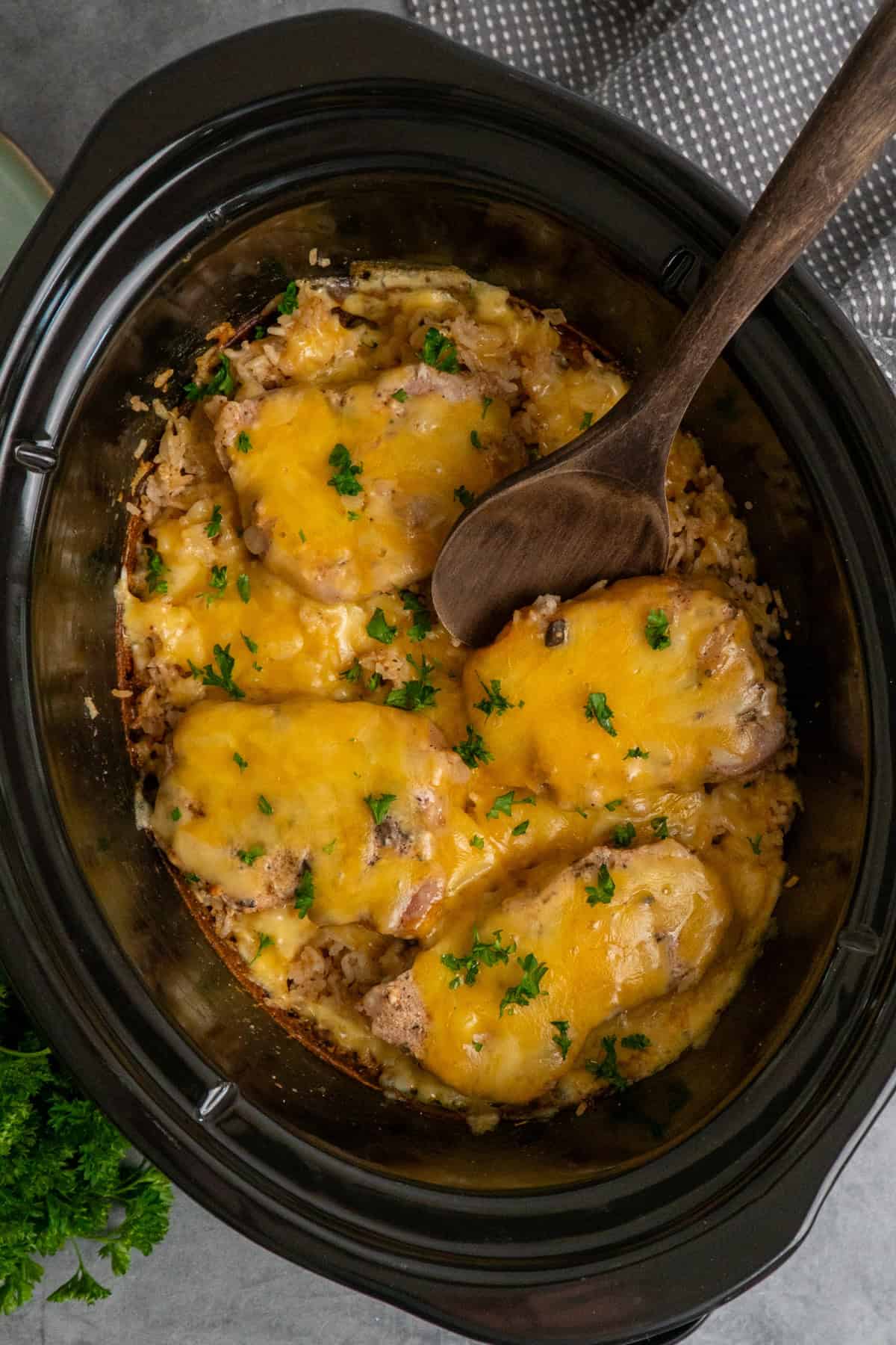Pork chops and rice in a crock pot covered with melted cheese and ready to be served.