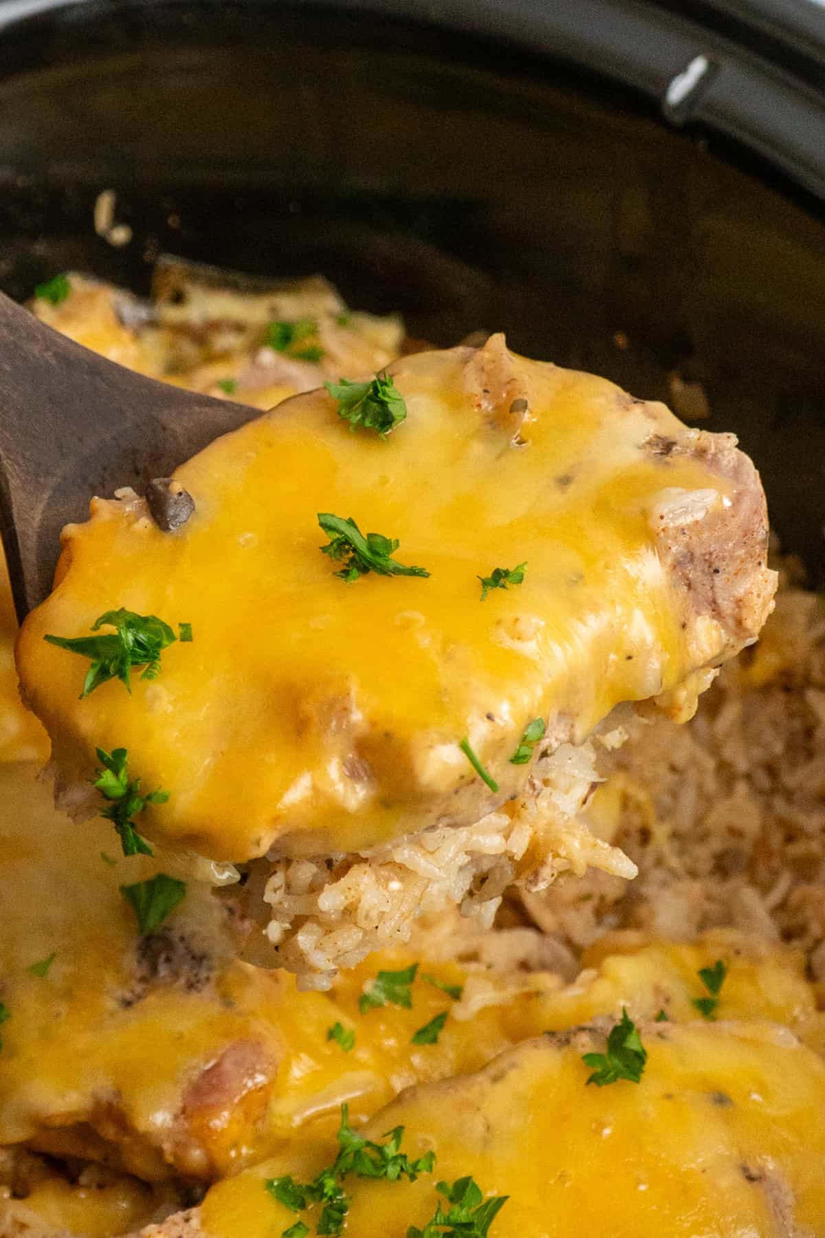 A wooden spoon holding a pork chop covered in cheese.