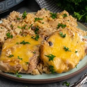 Crock pot pork chops and rice on a plate garnished with chopped parsley.