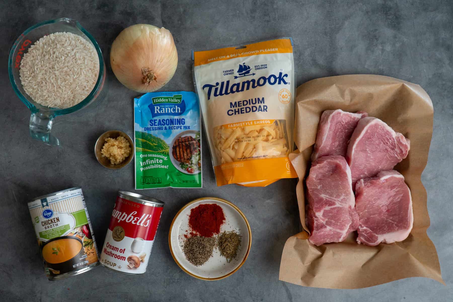 Ingredients to make pork chops and rice on a gray countertop.