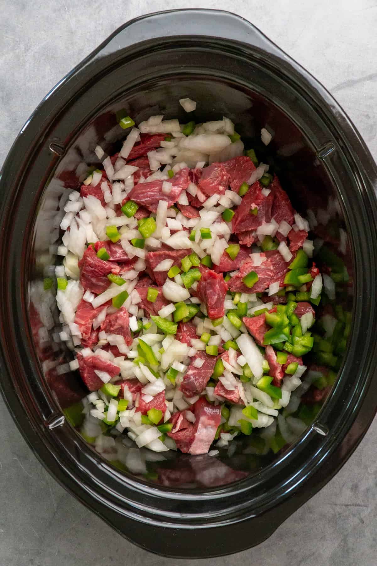 Stew meat, diced green peppers and diced onions in a crock pot.