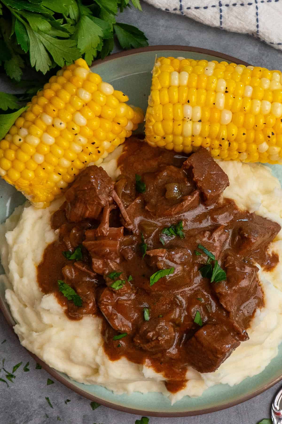 Crock pot steak and gravy over mashed potatoes with a side of corn on the cob.