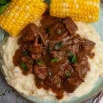Crock pot steak and gravy over mashed potatoes with a side of corn on the cob.