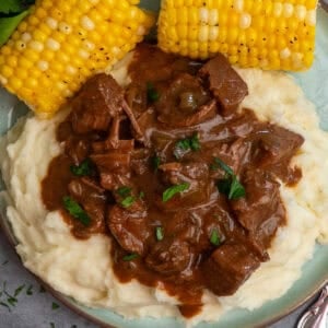 Crock pot steak and gravy over mashed potatoes with a side of corn on the cob.