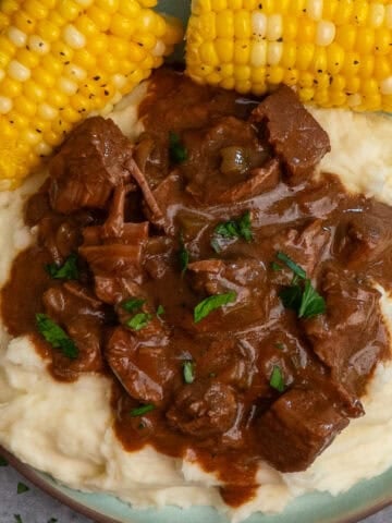 Crock pot steak and gravy over mashed potatoes with a side of corn on the cob.