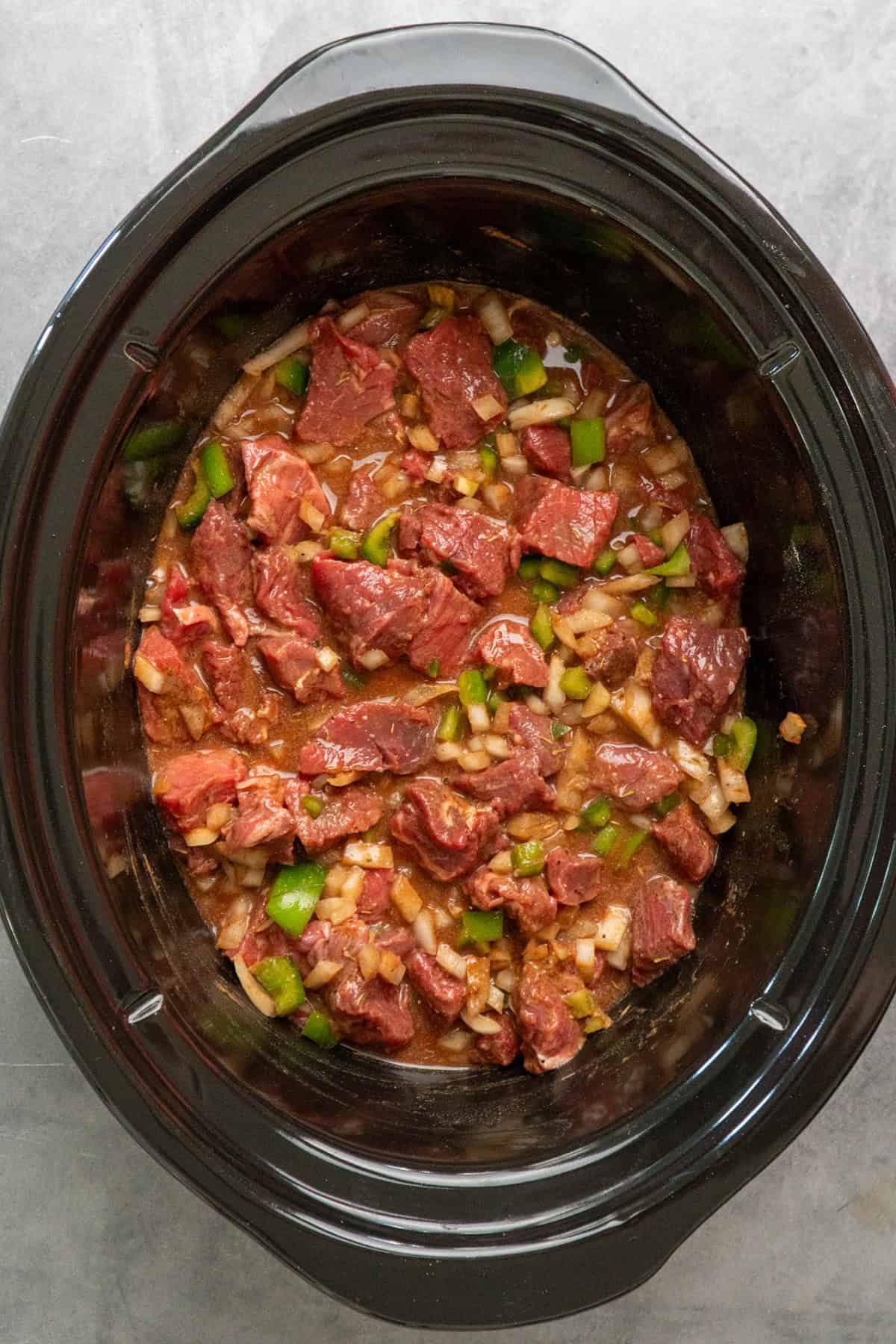 Steak, vegetables and gravy mixed together in a crock pot ready to be cooked.