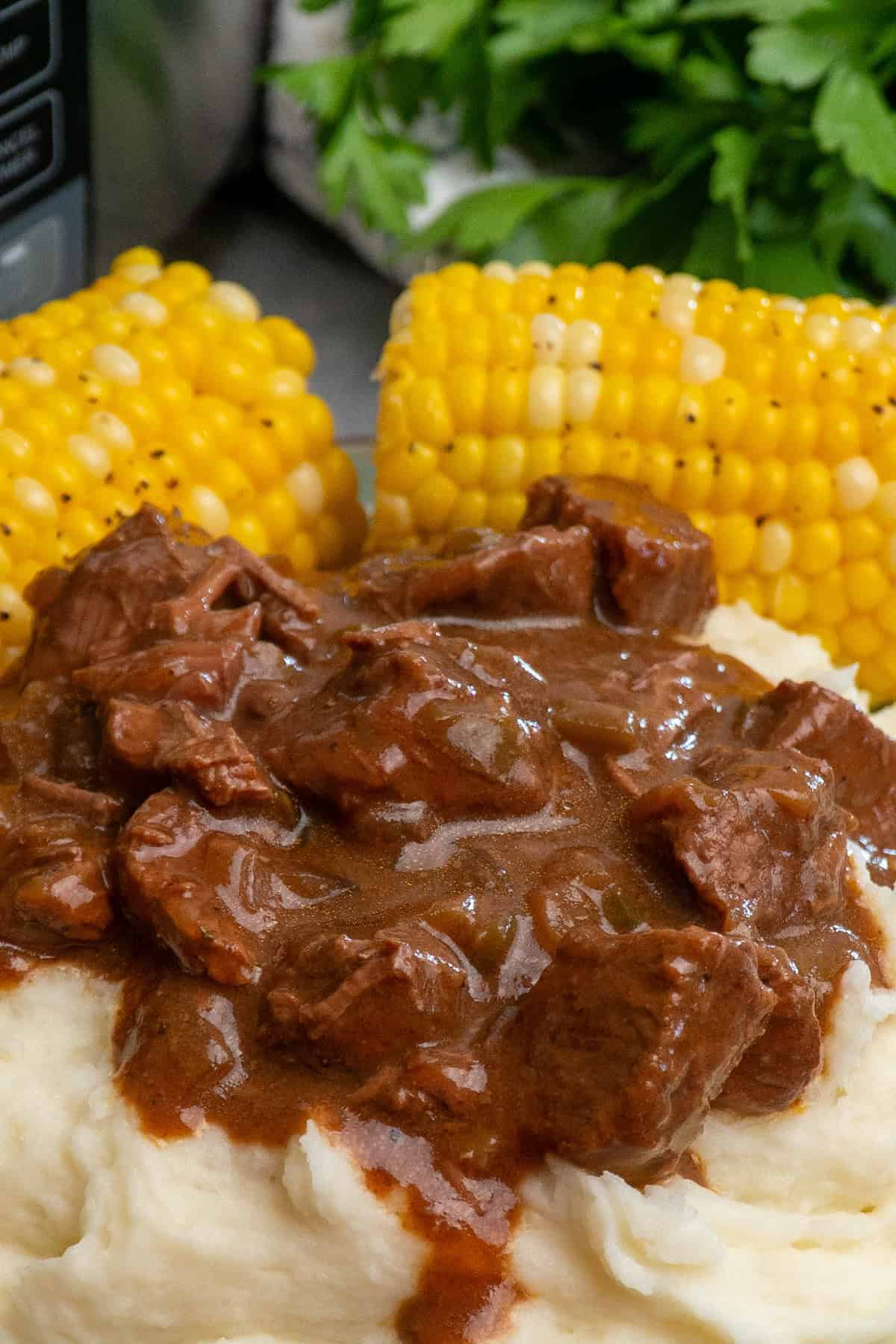 Steak and gravy over mashed potatoes over mashed potatoes with a side of corn.