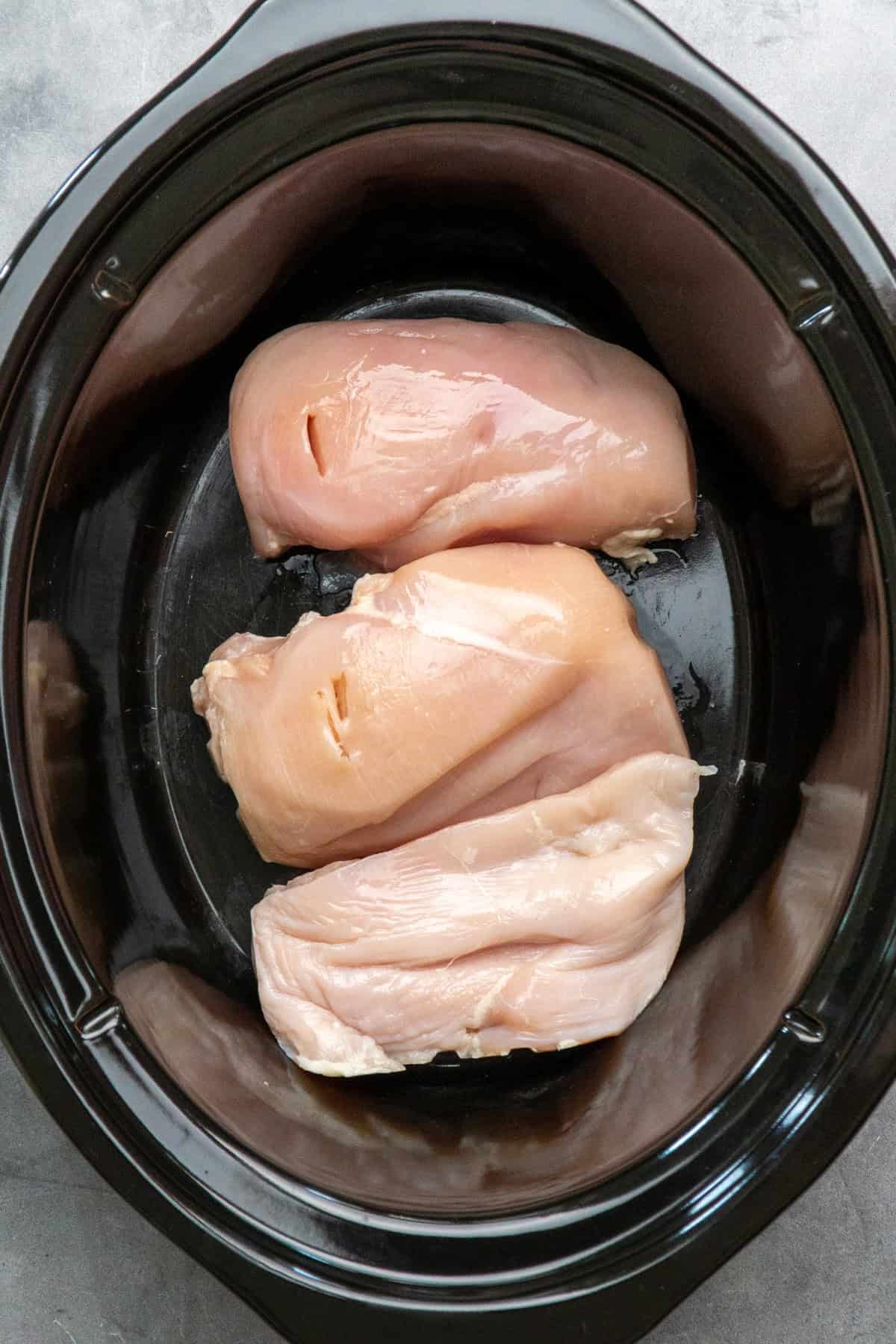 Chicken breasts on the bottom of a slow cooker.