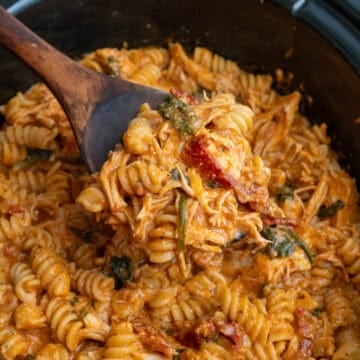 Crock pot tuscan chicken pasta being scooped with a wooden spoon.