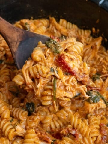 Crock pot tuscan chicken pasta being scooped with a wooden spoon.