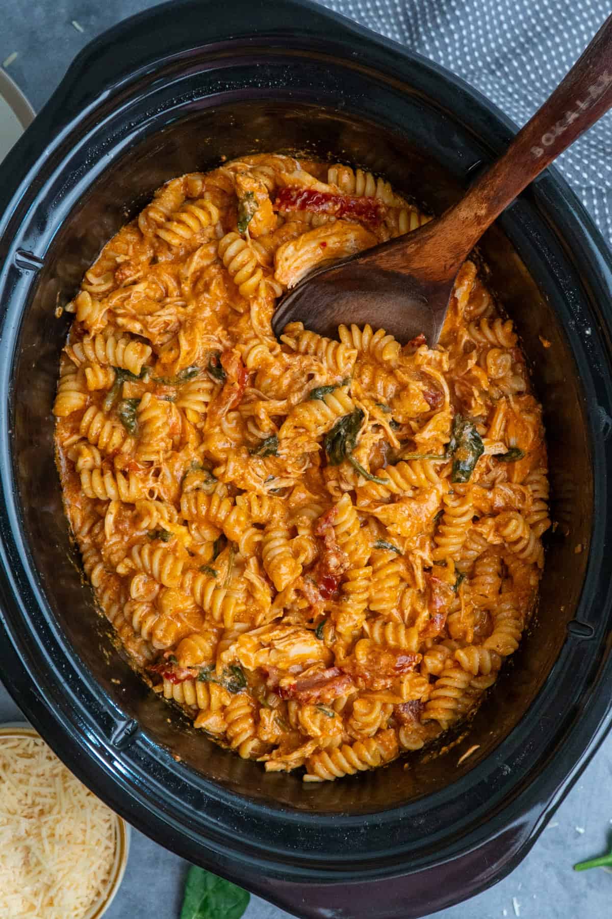 Crock pot tuscan chicken pasta being mixed with a wooden spoon.
