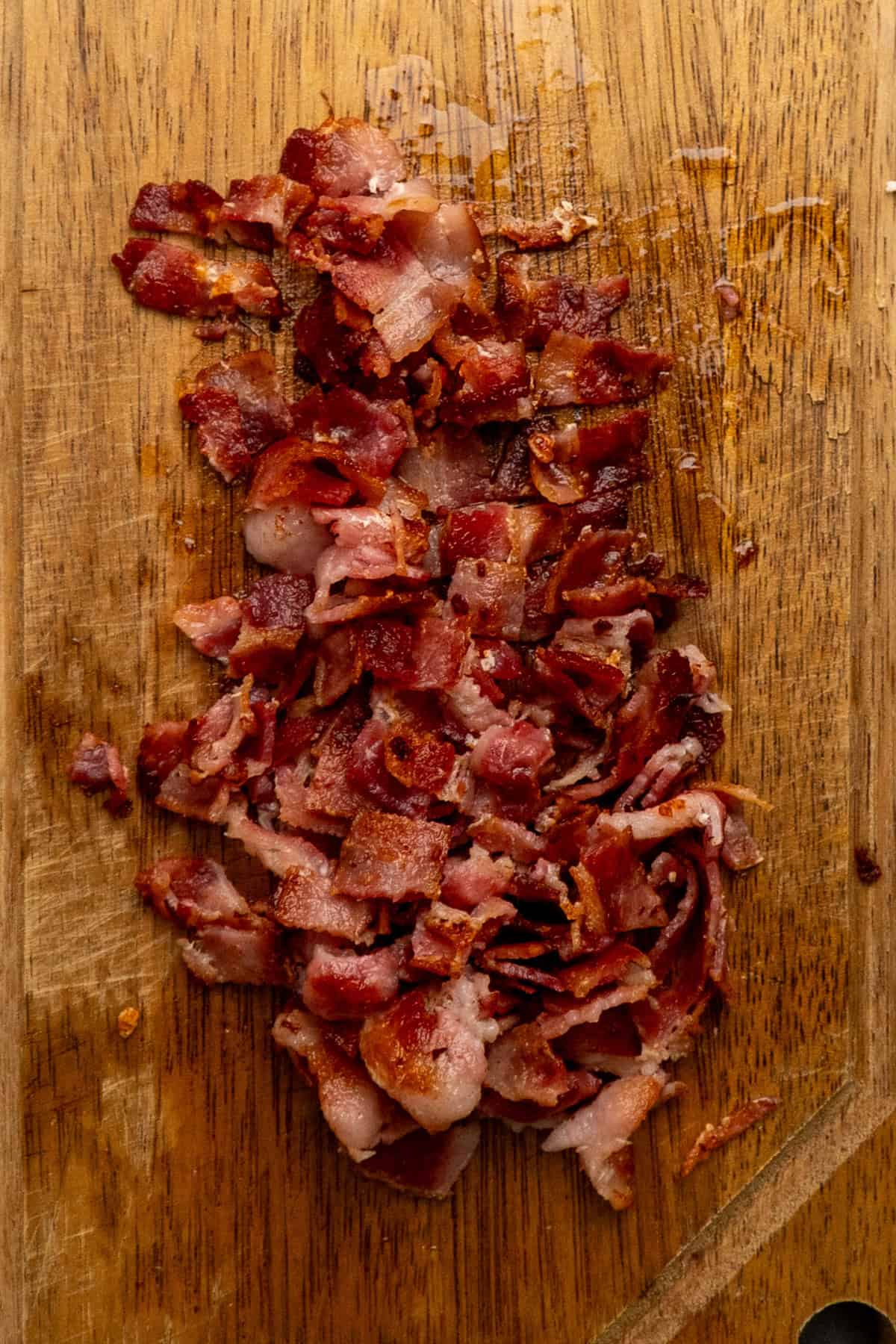 Cooked and chopped bacon on a wood cutting board.