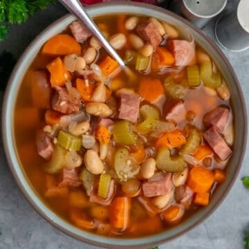 A bowl of ham and bean soup with a spoon in it.