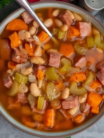 A bowl of ham and bean soup with a spoon in it.